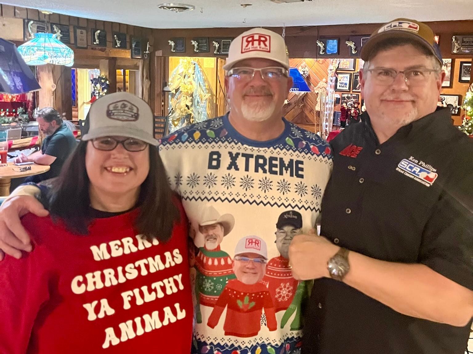 Three people holding a B Xtreme Christmas sweater at the Winter Wonderland Cookoff