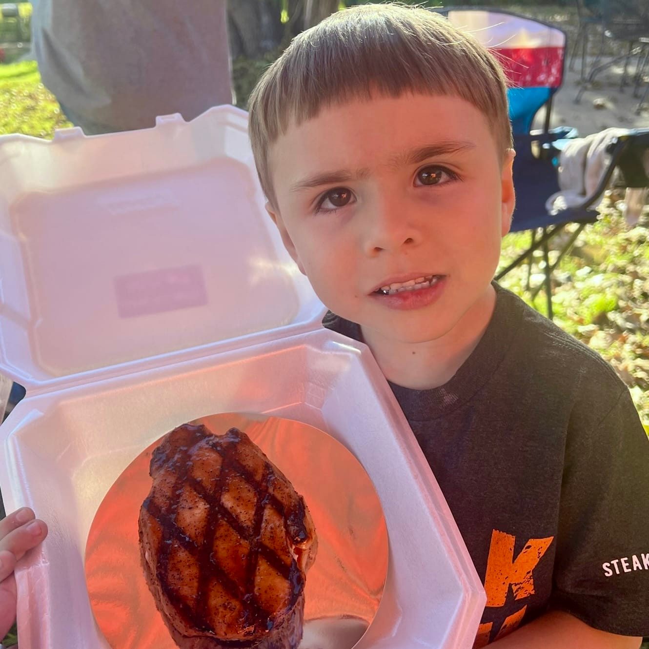 Young cook holding a grilled steak in a takeout box at the Winter Wonderland Cookoff